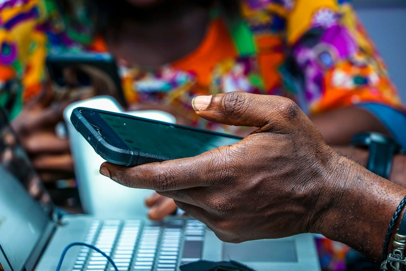 A hand holding a smartphone above a laptop